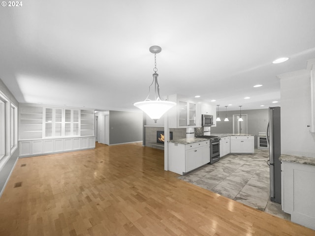 kitchen featuring stainless steel appliances, light stone countertops, white cabinetry, light tile floors, and pendant lighting