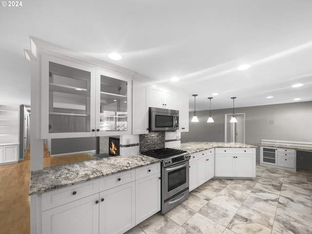 kitchen with kitchen peninsula, tasteful backsplash, white cabinetry, appliances with stainless steel finishes, and pendant lighting