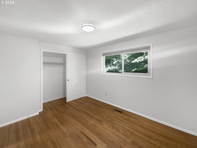 unfurnished bedroom with wood-type flooring, a closet, and a textured ceiling