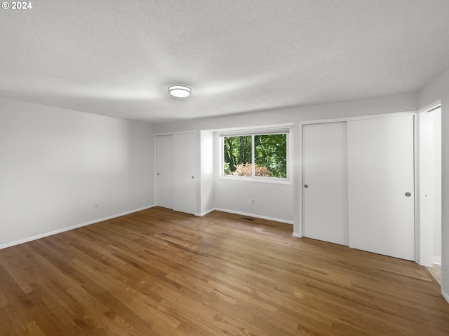 unfurnished bedroom with a textured ceiling, two closets, and wood-type flooring