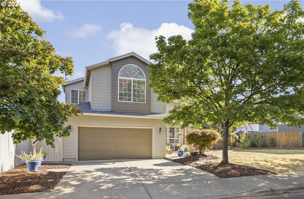 traditional-style house featuring a garage, concrete driveway, and fence