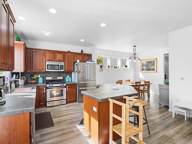 kitchen featuring hanging light fixtures, decorative backsplash, a kitchen island, stainless steel appliances, and light wood-type flooring