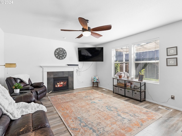 living room with a tile fireplace, light hardwood / wood-style floors, and ceiling fan