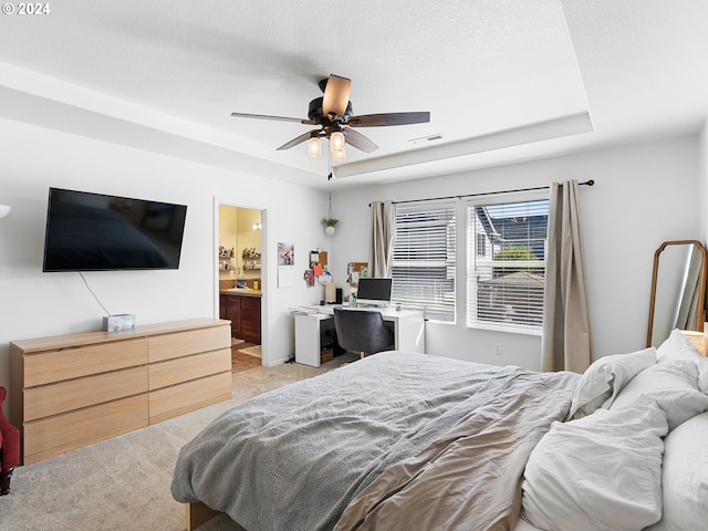 bedroom featuring ceiling fan, a textured ceiling, a tray ceiling, and connected bathroom