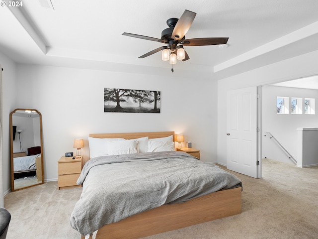 bedroom featuring a tray ceiling, light carpet, and ceiling fan