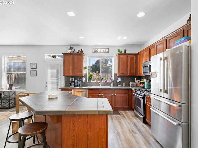 kitchen featuring appliances with stainless steel finishes, tasteful backsplash, light hardwood / wood-style flooring, tile counters, and sink