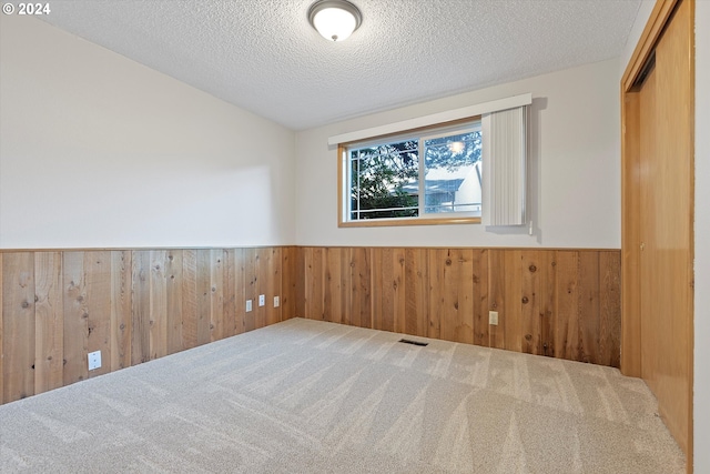 spare room with wood walls, a textured ceiling, and carpet floors