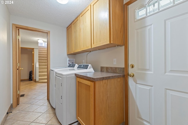 clothes washing area featuring a textured ceiling, washing machine and dryer, light tile patterned floors, and cabinets