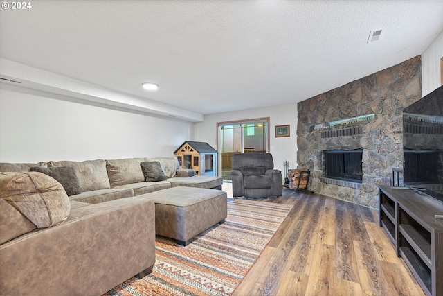 living room featuring a textured ceiling, a stone fireplace, and hardwood / wood-style flooring