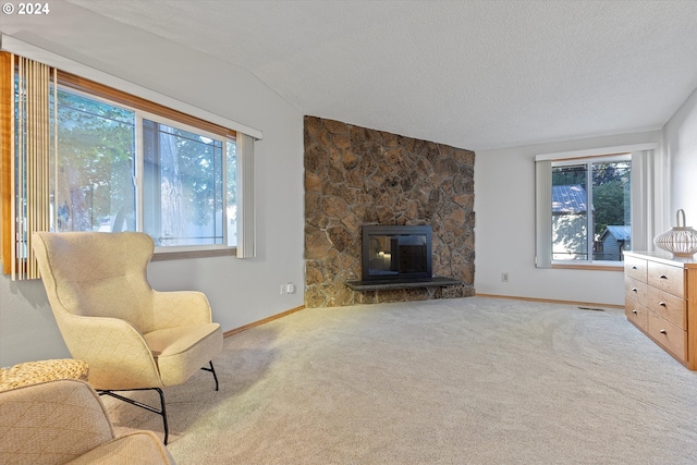 carpeted living room with vaulted ceiling, a textured ceiling, a healthy amount of sunlight, and a stone fireplace