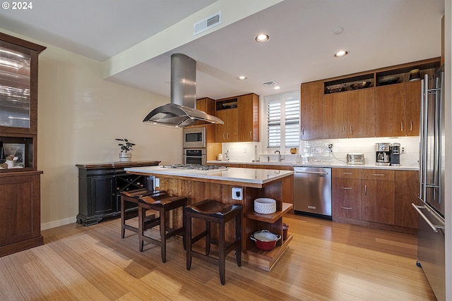 kitchen with light wood-type flooring, a breakfast bar, island range hood, stainless steel appliances, and a center island