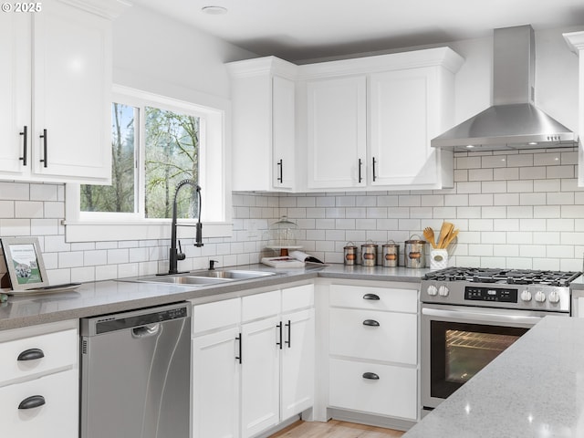 kitchen featuring stainless steel appliances, sink, white cabinets, decorative backsplash, and wall chimney range hood