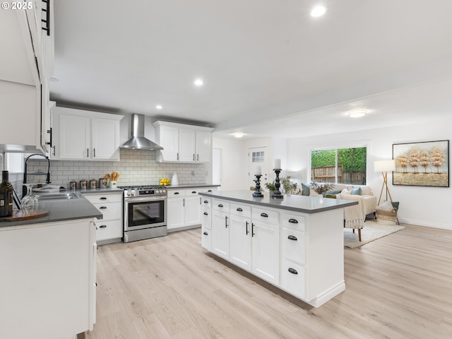 kitchen with gas range, wall chimney exhaust hood, a center island, white cabinetry, and sink