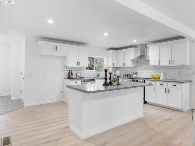 kitchen featuring a kitchen island, white cabinets, stainless steel dishwasher, and wall chimney exhaust hood