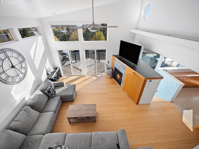 living room with light hardwood / wood-style flooring, a tiled fireplace, high vaulted ceiling, and ceiling fan