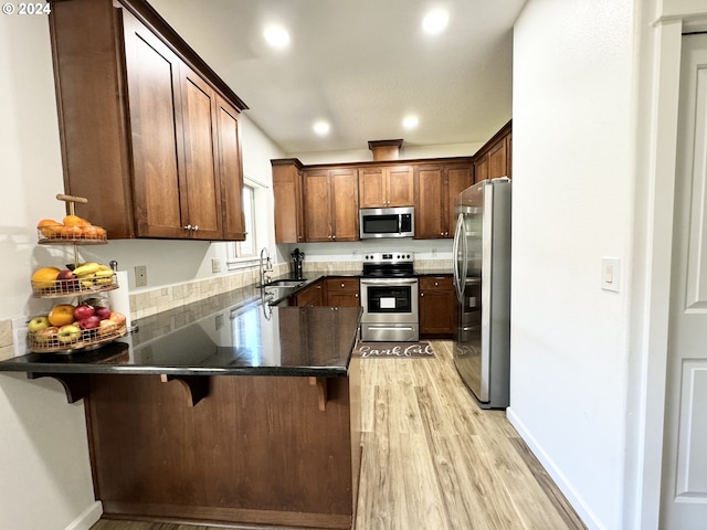 kitchen with light hardwood / wood-style flooring, kitchen peninsula, appliances with stainless steel finishes, and a kitchen bar