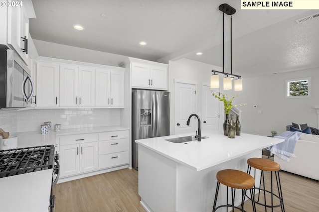 kitchen featuring white cabinets, an island with sink, sink, backsplash, and appliances with stainless steel finishes