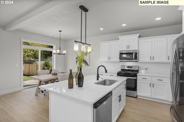 kitchen with an island with sink, stainless steel appliances, white cabinets, sink, and decorative light fixtures