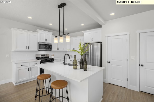 kitchen with light hardwood / wood-style floors, a center island with sink, stainless steel appliances, hanging light fixtures, and white cabinets