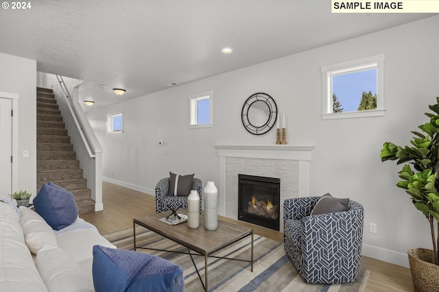 living room featuring a textured ceiling, a wealth of natural light, a tile fireplace, and light hardwood / wood-style flooring