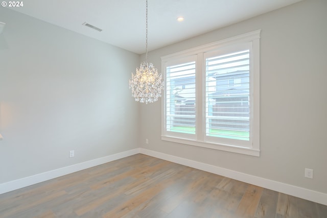 empty room featuring wood-type flooring and an inviting chandelier