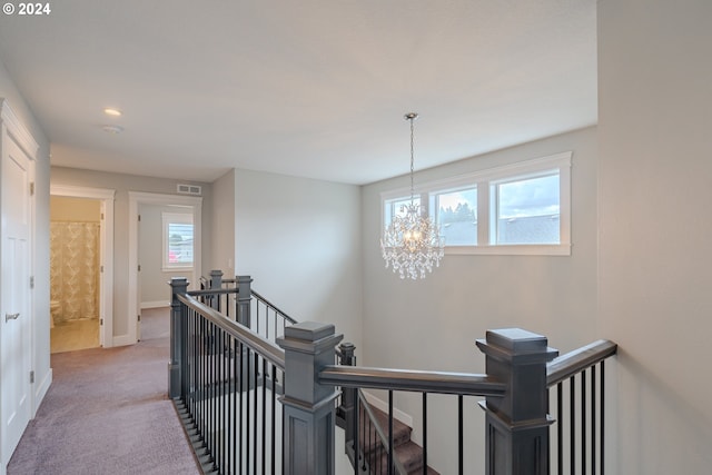 hallway featuring light colored carpet, a wealth of natural light, and a chandelier