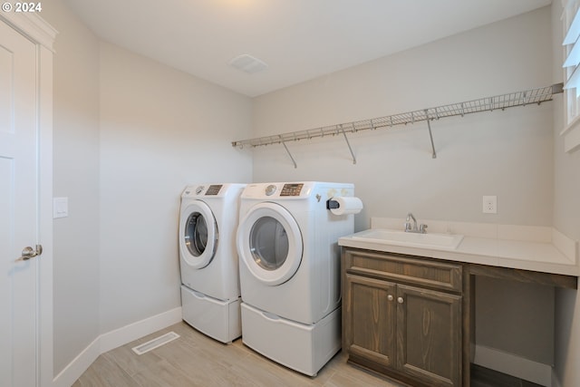 laundry area with sink, cabinets, light hardwood / wood-style flooring, and washing machine and clothes dryer