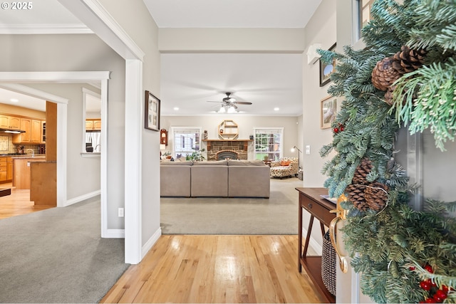 living room with light hardwood / wood-style floors, a stone fireplace, ceiling fan, and ornamental molding