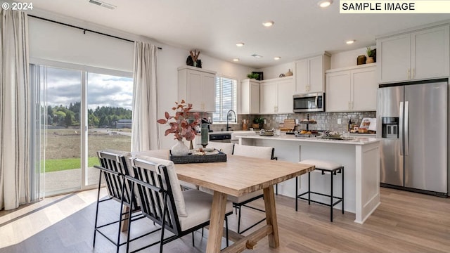 kitchen featuring light wood-style flooring, appliances with stainless steel finishes, light countertops, and backsplash