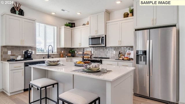 kitchen with a kitchen breakfast bar, a center island, stainless steel appliances, white cabinetry, and a sink