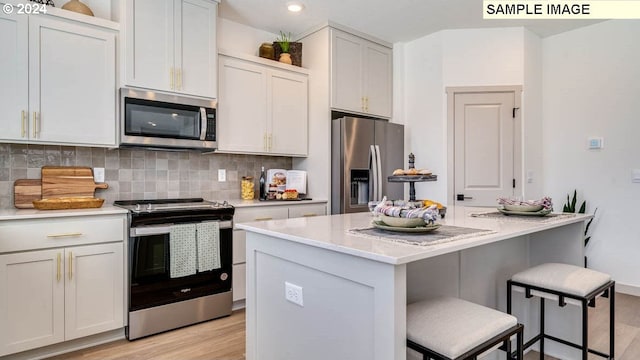 kitchen with a kitchen island, appliances with stainless steel finishes, decorative backsplash, light wood finished floors, and a kitchen bar