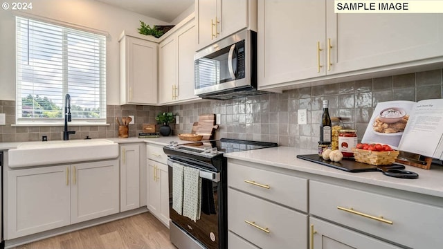 kitchen with tasteful backsplash, light wood-style flooring, appliances with stainless steel finishes, light countertops, and a sink