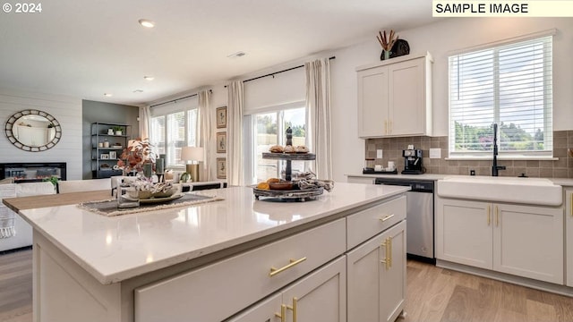 kitchen with a center island, light wood finished floors, a large fireplace, a sink, and dishwasher