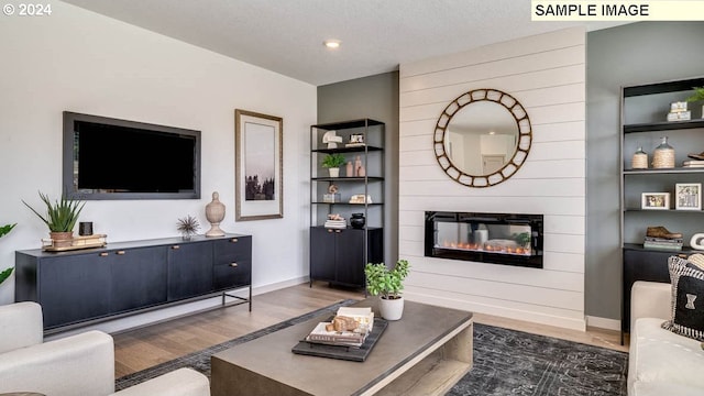 living room featuring a large fireplace, a textured ceiling, baseboards, and wood finished floors