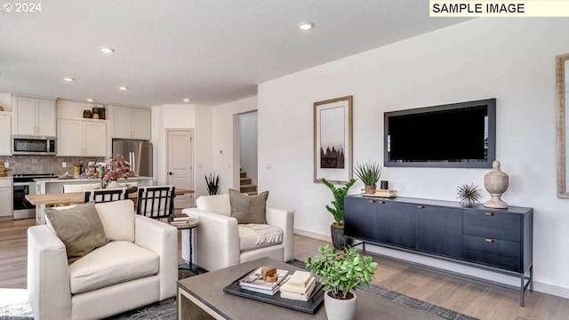 living area with baseboards, stairway, light wood-style flooring, and recessed lighting