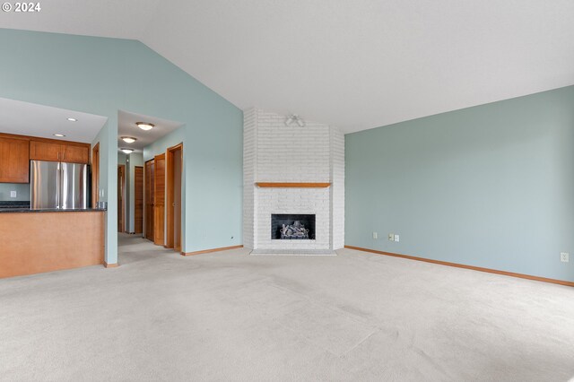 unfurnished living room with light carpet, a fireplace, high vaulted ceiling, and brick wall