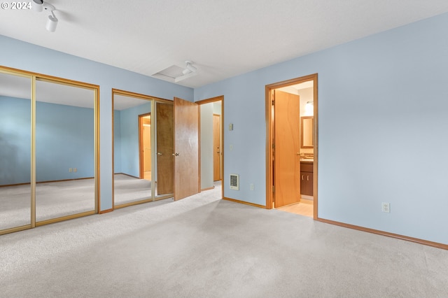 unfurnished bedroom featuring light carpet, visible vents, baseboards, multiple closets, and attic access