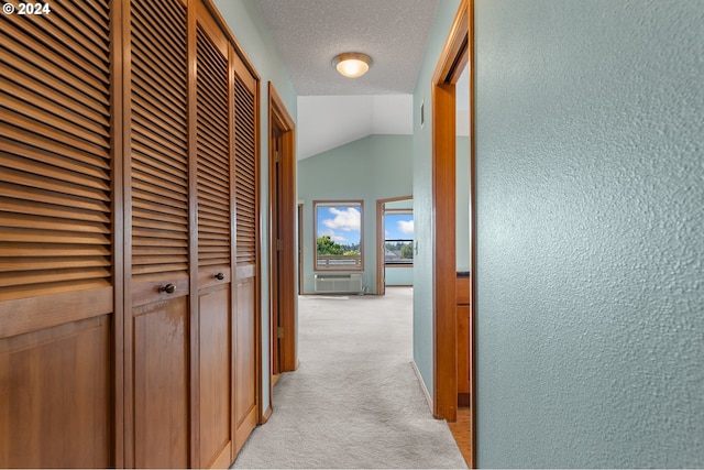 corridor featuring light carpet, a textured wall, vaulted ceiling, and a textured ceiling