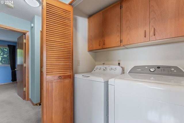 clothes washing area with washer and dryer, cabinet space, light carpet, and a textured ceiling