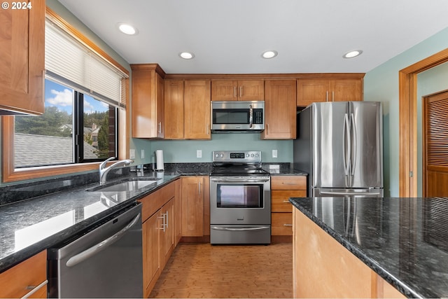 kitchen with stainless steel appliances, dark stone countertops, a sink, and recessed lighting