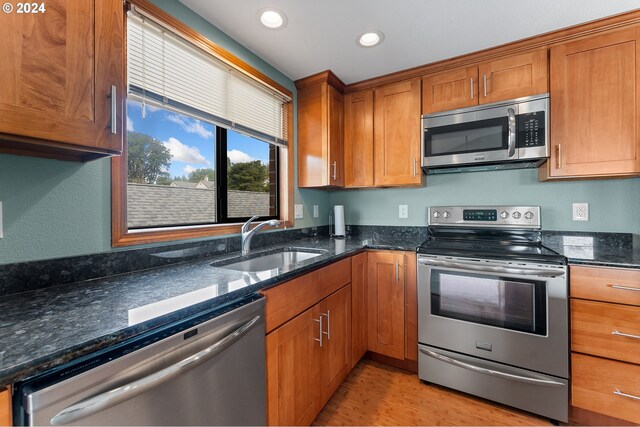 kitchen with sink, light wood-type flooring, dark stone counters, and stainless steel appliances