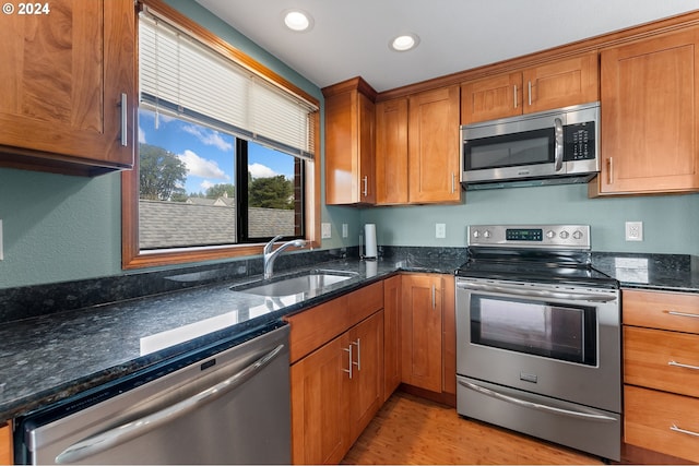 kitchen featuring brown cabinets, appliances with stainless steel finishes, dark stone counters, and a sink