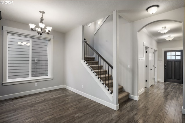 foyer entrance with an inviting chandelier, a textured ceiling, crown molding, and dark hardwood / wood-style flooring