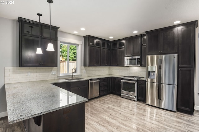 kitchen featuring sink, kitchen peninsula, hanging light fixtures, light hardwood / wood-style flooring, and stainless steel appliances