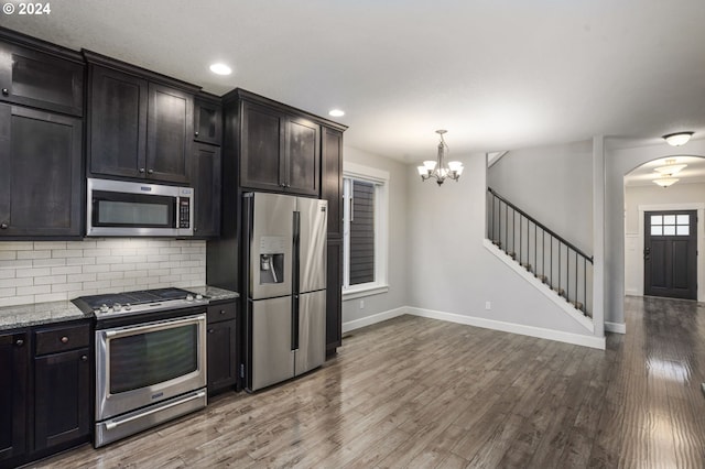 kitchen with light stone countertops, pendant lighting, stainless steel appliances, an inviting chandelier, and hardwood / wood-style floors