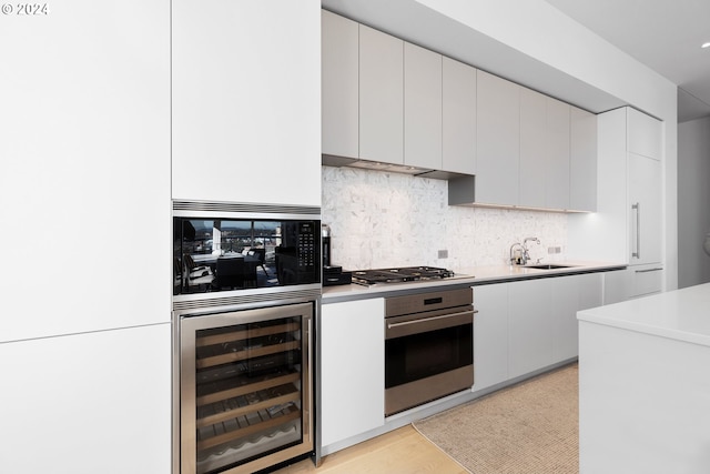 kitchen with white cabinets, tasteful backsplash, beverage cooler, appliances with stainless steel finishes, and sink