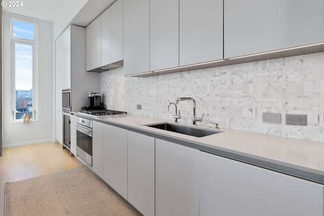 kitchen with light hardwood / wood-style flooring, stainless steel appliances, sink, white cabinets, and tasteful backsplash