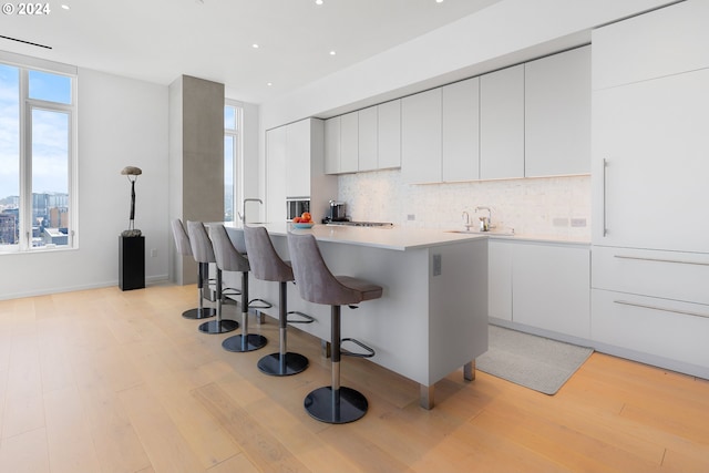 kitchen featuring backsplash, white cabinetry, a kitchen island with sink, light hardwood / wood-style flooring, and sink