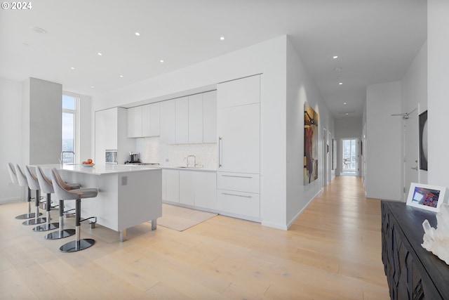 kitchen featuring backsplash, a kitchen island, a breakfast bar, white cabinetry, and light wood-type flooring