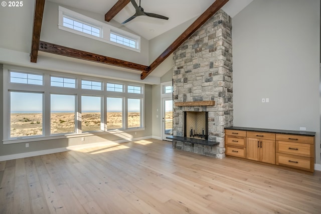 unfurnished living room with a stone fireplace, high vaulted ceiling, beamed ceiling, ceiling fan, and light hardwood / wood-style flooring